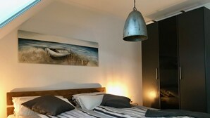 Un dormitori amb un llit, almoinos, una làmpada penjant, un armari i un quadre a la paret.