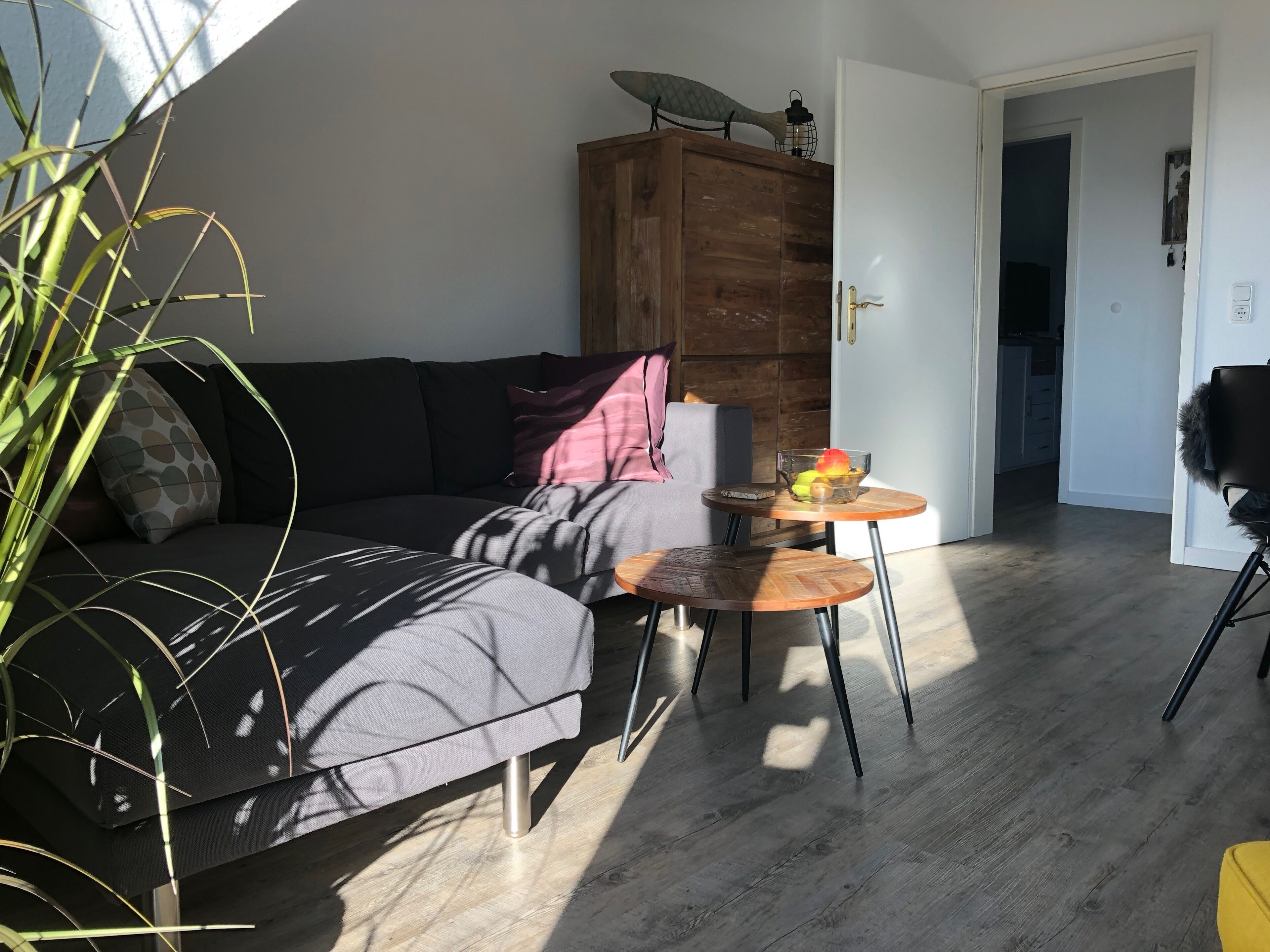 Een moderne woonkamer met een donkergrijze bank, een houten kast en een kleine ronde tafel met een schaal fruit.