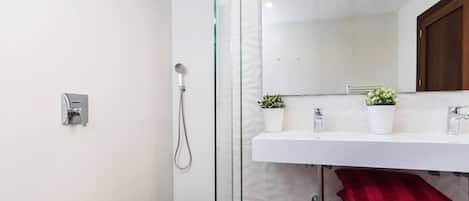 Une salle de bain moderne avec une douche en verre, un lavabo blanc agrémenté de deux plantes en pot et une serviette rouge.