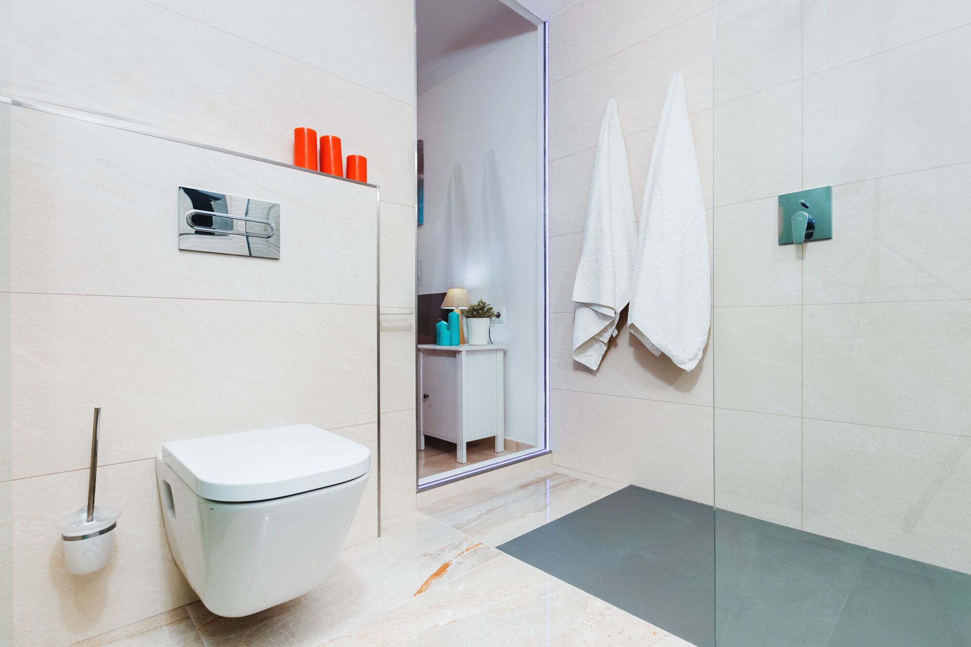 Une salle de bain moderne équipée de toilettes, d’une douche et d’un lavabo. Des serviettes sont accrochées au mur, et une petite étagère contient des articles de toilette.