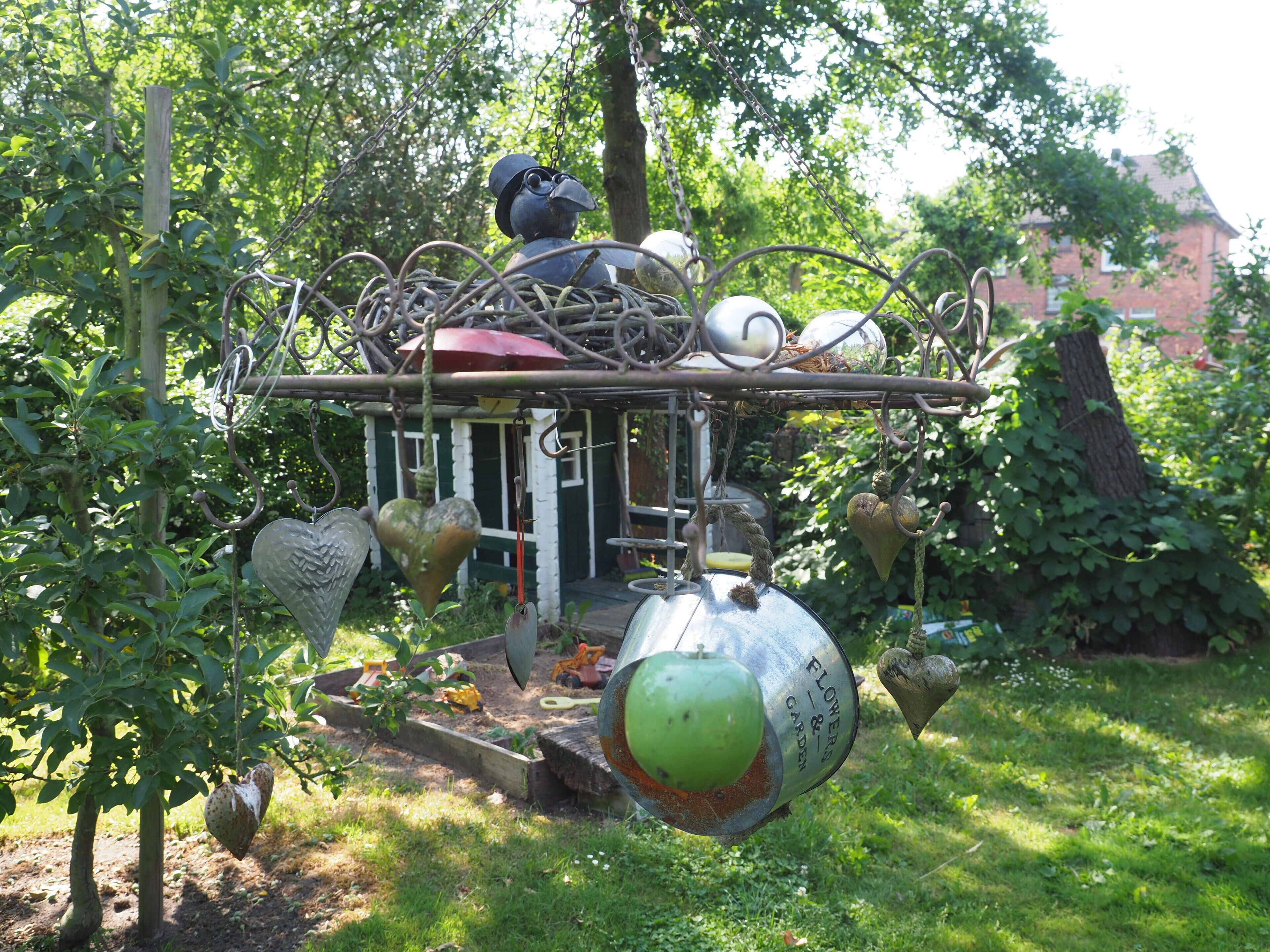 A garden with a metal structure featuring various objects like a heart-shaped ornament, a green apple, and a metal pot.