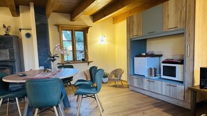 Una cocina acogedora con armarios de madera, un comedor con sillas color turquesa y un ventanal con vistas a árboles.