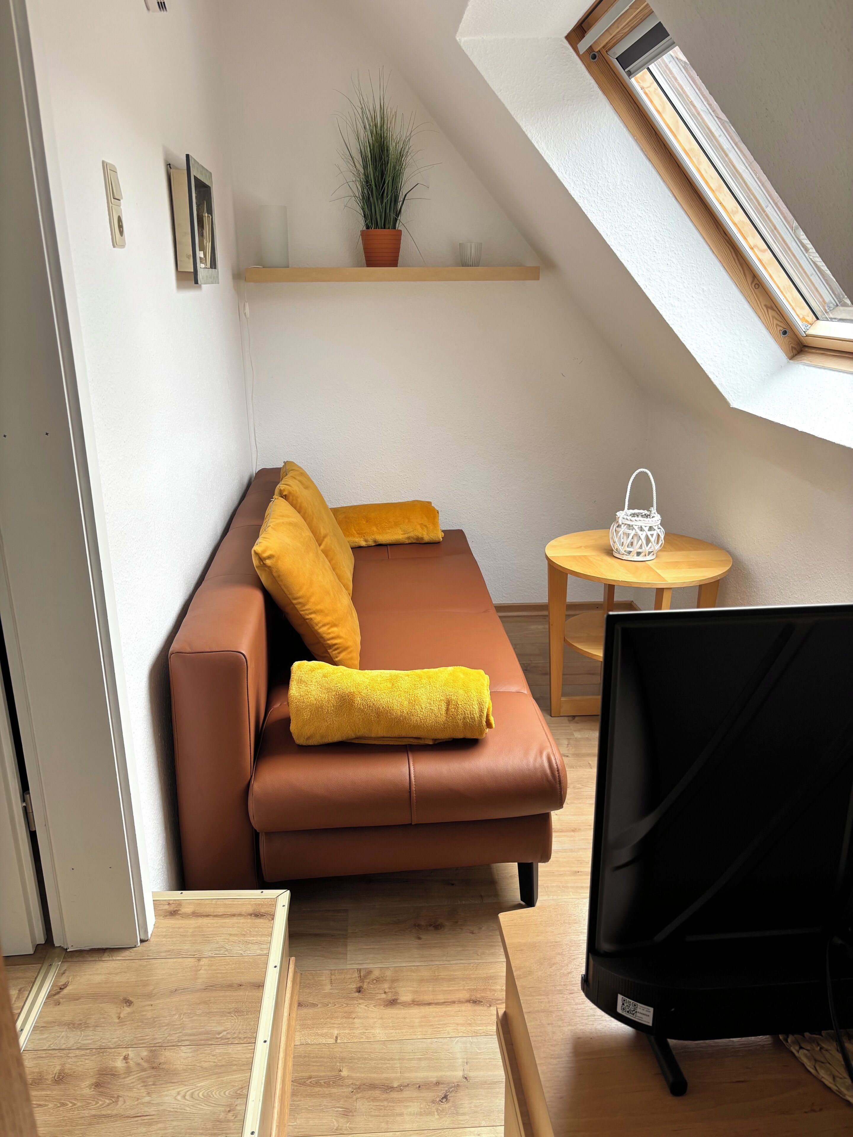 Un espace de vie moderne avec un canapé marron, des coussins jaunes, une petite table sur laquelle est posée une lanterne blanche, et une plante en pot.