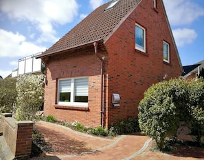 A red brick house with a tiled roof, a front window with shutters, and a small garden with a pathway leading to the entrance.