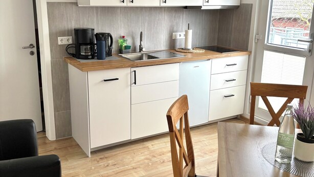 A modern kitchen with white cabinets, a coffee maker, and a sink. There is a dining table with chairs and a potted plant. - Apartment 3 with balcony, animal free  near the south beach (Borkum)