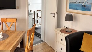 A room with a wooden dining table, a black sofa, a framed picture, and a television mounted on the wall. - Apartment 3 with balcony, animal free  near the south beach (Borkum)