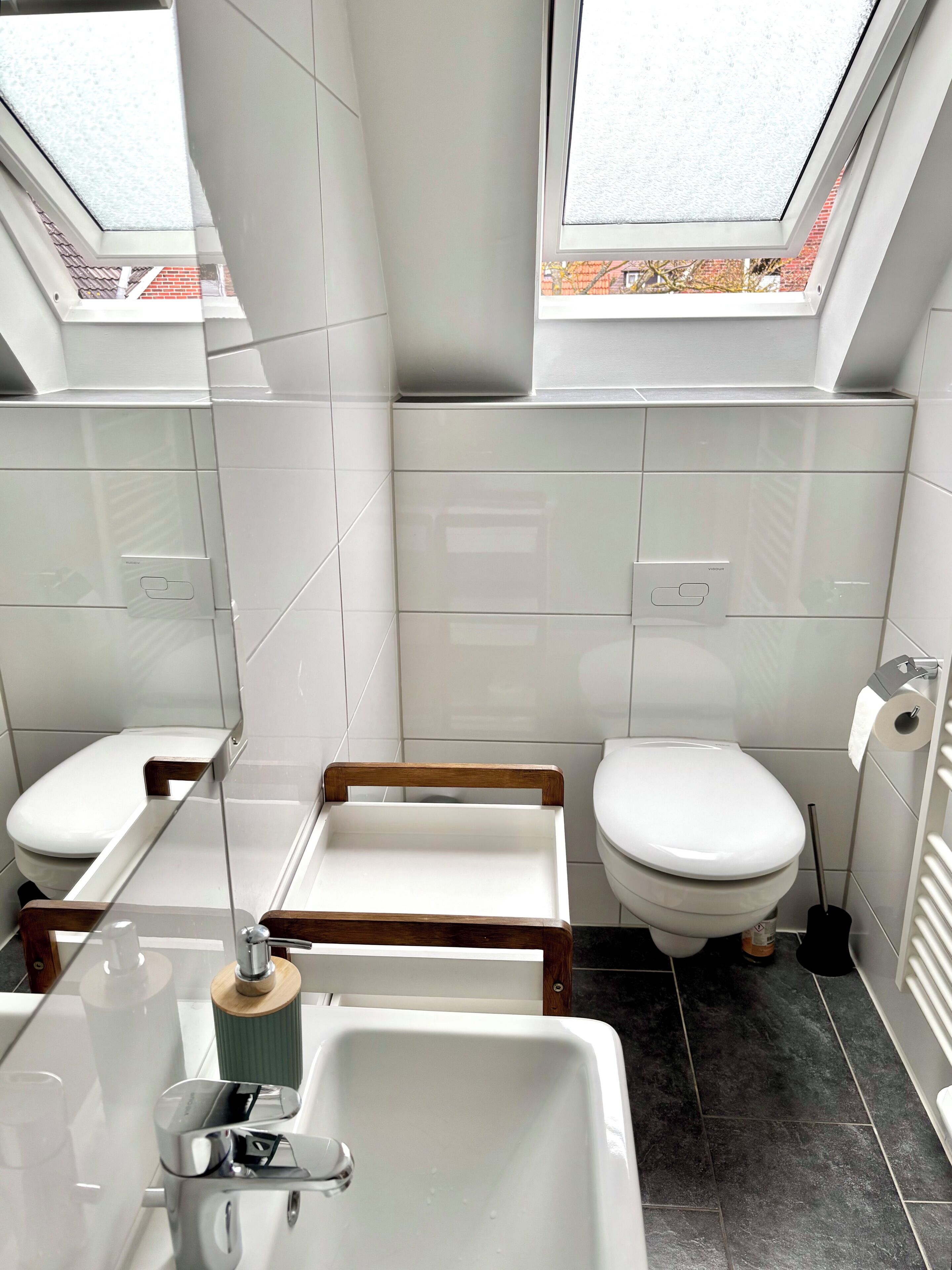 A modern bathroom with a skylight, white tiles, a wooden vanity, a white toilet, and a sink with a mirror.