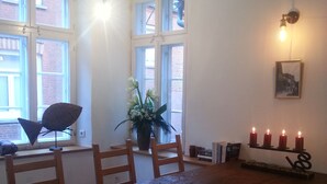 Un comedor con una mesa de madera, cuatro sillas, una planta en maceta, un estante con velas y un cuadro enmarcado.