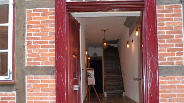 Una puerta roja con un panel de vidrio que muestra el número 101, que da a una escalera y un caballete con una pintura.