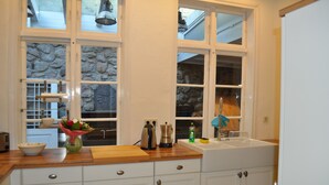Una cocina con armarios blancos, encimera de madera, pared de piedra y ventana con vistas.