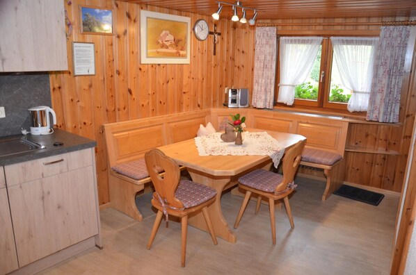 A wooden-paneled room with a dining table, chairs, a clock, and a window with curtains. - Freiburg, Southern Black Forest, Schauinsland Hofsgrund, farm houses, (Oberried)
