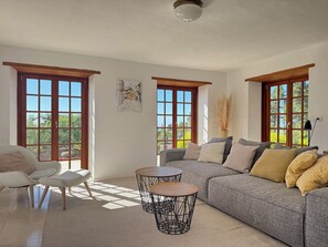 A spacious living area with a large gray sofa, two round tables, and a white chair.