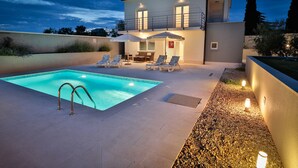 Ein modernes, zweistöckiges Haus mit Pool, Sitzgelegenheit im Freien und einer gut beleuchteten Terrassenfläche.