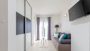 Ein modernes Wohnzimmer mit einer Couch, einem Flachbildfernseher und einem kleinen Tisch, belegt mit einem flauschigen, weißen Teppich.