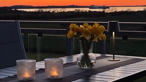 Una mesa con velas y un jarrón de flores, con vista a una puesta de sol sobre el agua.