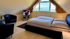 Un dormitorio con cama, televisor, sillón y ventana con cortinas.