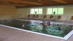 Una piscina interior con vigas de madera, suelo de baldosas y varias personas nadando.