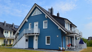 A two-story house with a blue exterior, a balcony, and a small porch area. - Beautiful apartment! 250 m to the Baltic Sea beach. Standing vacation, short trip or mobile working. (Börgerende-Rethwisch)