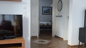 A living room with a TV, wooden furniture, a red chair, and a dining table with a glass and a plate. - Beautiful apartment! 250 m to the Baltic Sea beach. Standing vacation, short trip or mobile working. (Börgerende-Rethwisch)