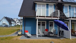 A two-story house with a balcony, a patio with outdoor furniture, and a solar panel on the roof. - Beautiful apartment! 250 m to the Baltic Sea beach. Standing vacation, short trip or mobile working. (Börgerende-Rethwisch)