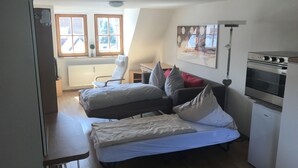 A compact room with a bed, a chair, a small table, and a kitchenette. - Wendlers Ferienwohnungen 2 (Schwaig bei Nuernberg)