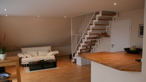 A modern living room with a wooden floor, a white sofa, a wooden coffee table, and a staircase with white railings. - Wendlers Ferienwohnungen 2 (Schwaig bei Nuernberg)