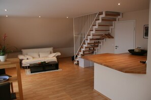 Een moderne woonkamer met een houten vloer, een witte bank, een houten salontafel en een trap met witte leuningen.
