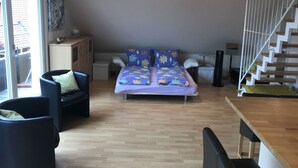 A bedroom with a bed, two chairs, a desk, a radiator, and a staircase. - Wendlers Ferienwohnungen 2 (Schwaig bei Nuernberg)