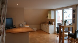 A modern kitchen with a wooden countertop, a sink, and cabinets. There is a dining area with two chairs and a small table. A television is mounted on the wall, and a clock is visible on the countertop. - Wendlers Ferienwohnungen 2 (Schwaig bei Nuernberg)