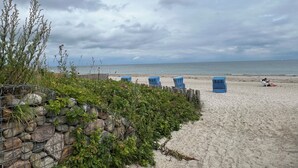 Une plage avec un mur de pierres, des chaises bleues et une personne assise sur le sable.