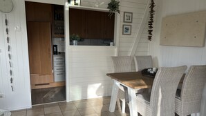 Un coin repas avec une table en bois et des chaises en osier, une cuisine avec des meubles en bois et un mur blanc orné de tableaux encadrés.