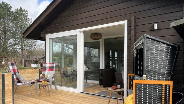 Une terrasse en bois avec des meubles d’extérieur, une porte-fenêtre coulissante donnant sur un espace de vie et une grande fenêtre.
