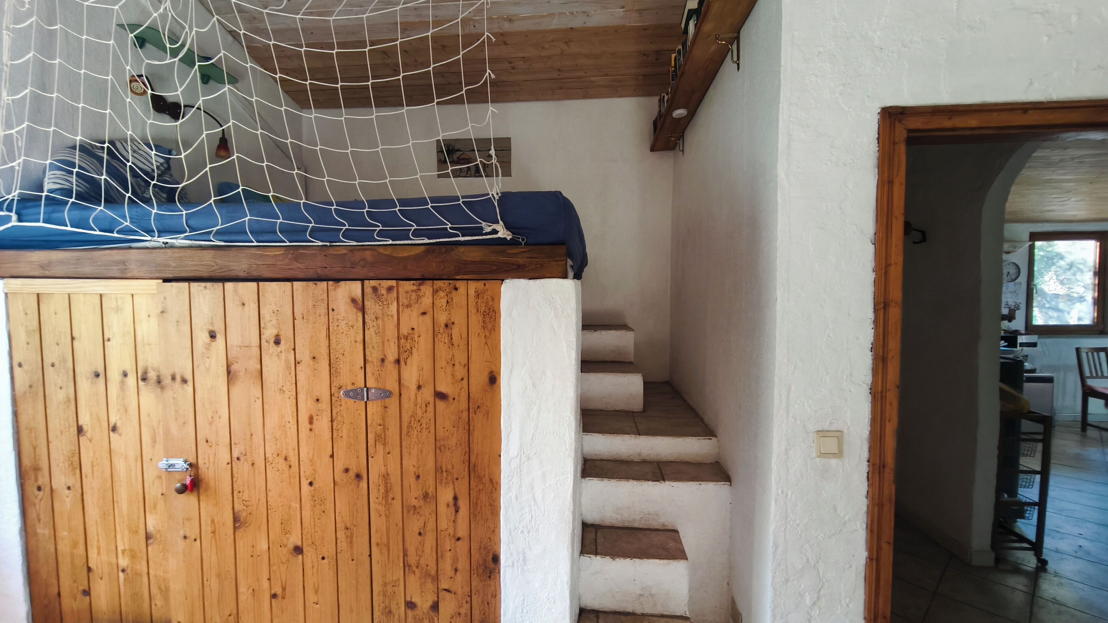 Una escalera de madera conduce a un dormitorio con una cama y un área cubierta por un mosquitero.