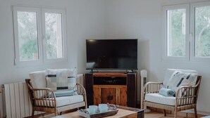 A spacious living room with a wooden ceiling, a large flat-screen TV, wicker chairs, a coffee table, and a bed with a blue cover. - Small but nice finca with great views and pool near Cala Ratjada (Capdepera)