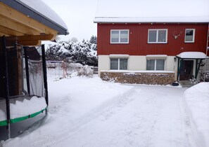 Una casa roja con techo nevado, un porche de madera y un muro de piedra.