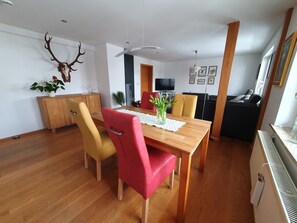 Un comedor con una mesa de madera, sillas rojas y amarillas, un jarrón con flores y una decoración de cráneo de ciervo montado en la pared.