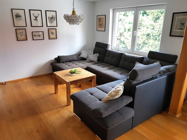 Ein modernes Wohnzimmer mit einer Eckcouch, einem Holztisch und gerahmten Kunstwerken an den Wänden.