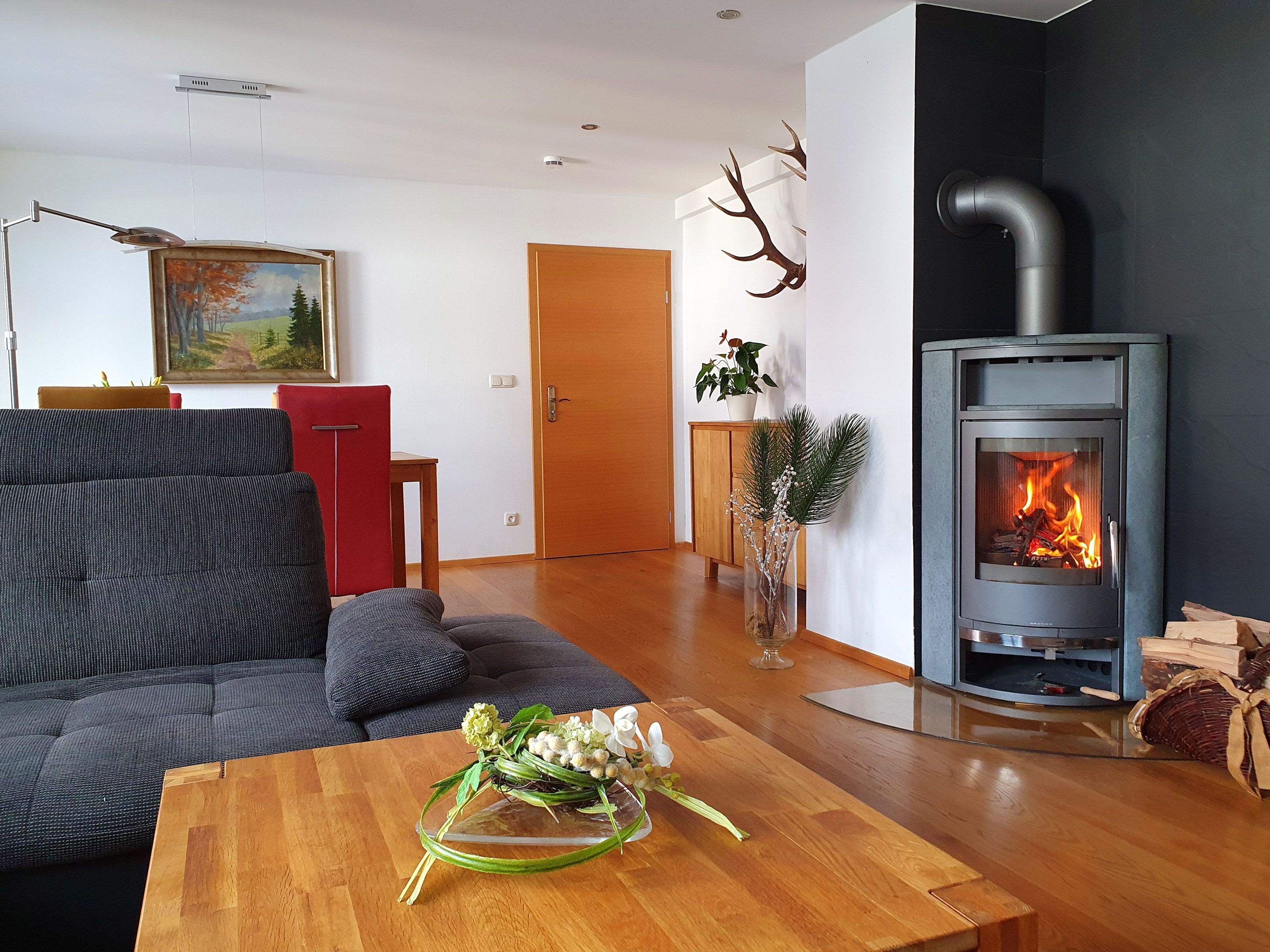 A modern living room with a sofa, a wooden coffee table with a vase, a fireplace, and a door leading to another room.