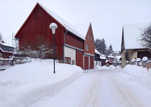 Uma rua coberta de neve com um celeiro vermelho e casas.