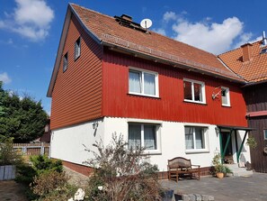 Ein rotes und weißes Haus mit geneigtem Dach, einer Satellitenschüssel und einer Bank davor.