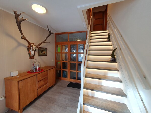 A staircase with wooden steps and a handrail, a wooden cabinet with drawers, a glass door with frosted glass panels, and a wall-mounted deer antler.