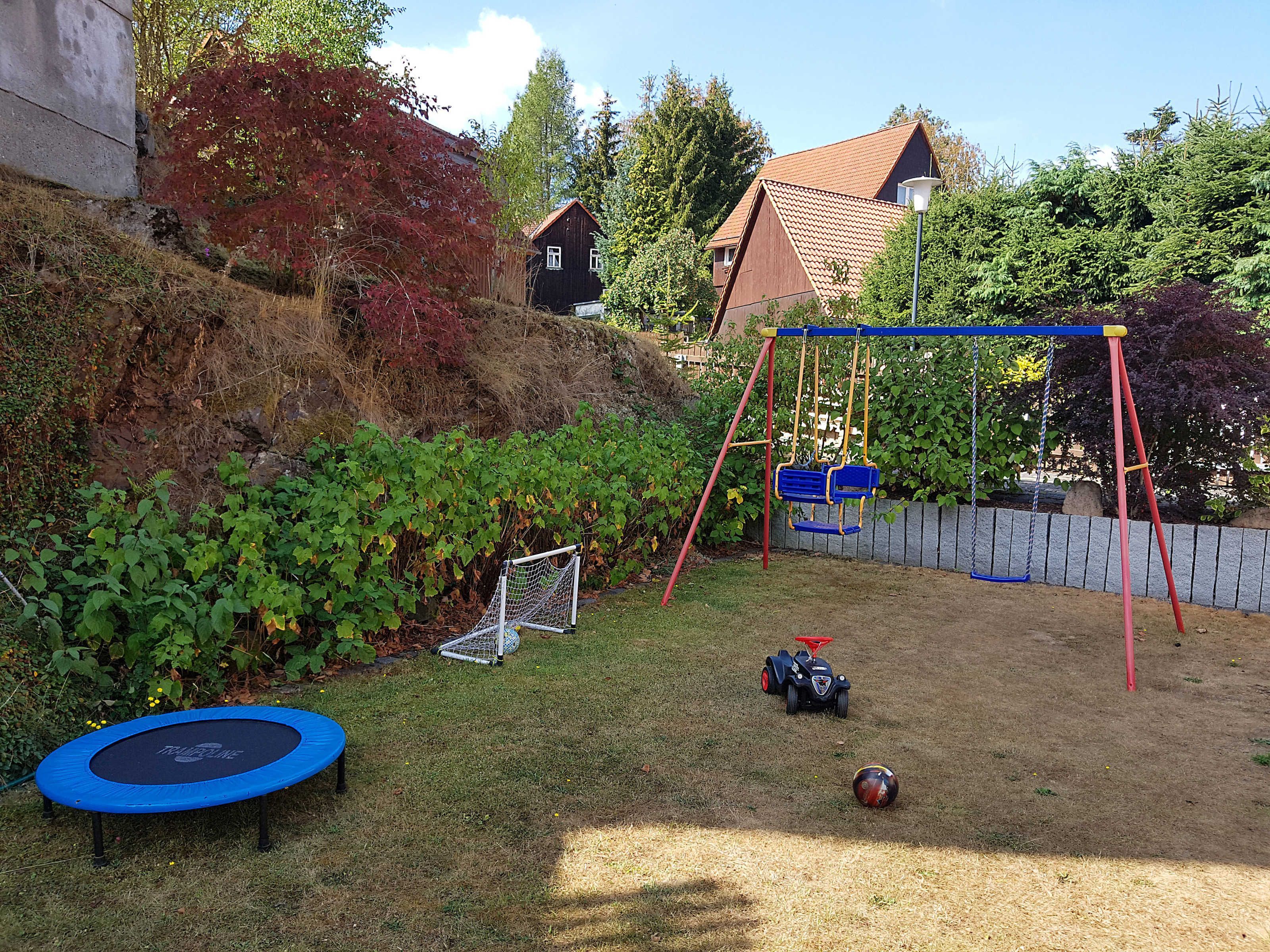 Ein Garten mit Trampolin, Schaukel, Fußballtor und einem Spielzeugauto.