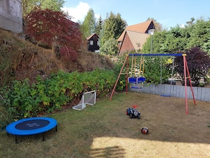 A backyard with a trampoline, swing set, soccer goal, and a toy car.