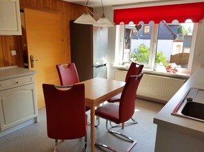 Eine kleine Küche mit Esstisch und Stühlen, ein Fenster mit Blick ins Freie und eine Wand in Rot.