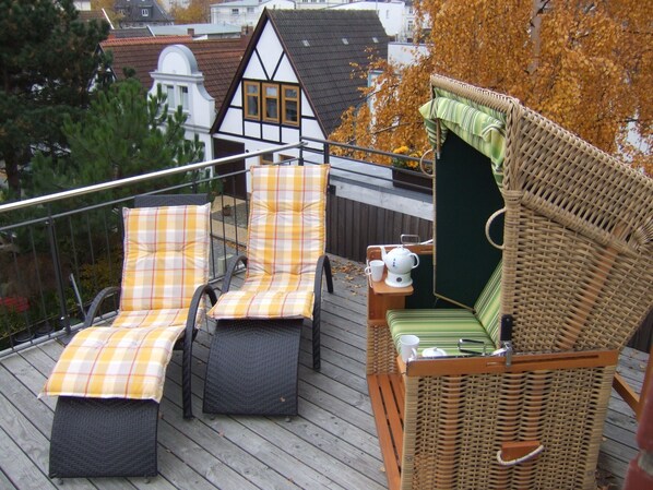 A deck with wicker chairs and a small table with a teapot and cup.