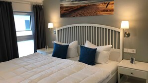 A neatly made bed with white and blue pillows, a white headboard, and a bedside table with a lamp. - Upper deck 2.06, Germany (Glowe auf Rügen)