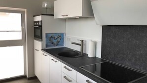 A modern kitchen with white cabinets, a black countertop, a built-in stove, and a window. - Upper deck 2.06, Germany (Glowe auf Rügen)