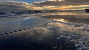 Ein Strand mit feuchtem Sand und sanften Wellen, unter einem bewölkten Himmel.