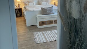 Un dormitorio con una cama, mesitas de noche, una lámpara, una alfombra y una planta.
