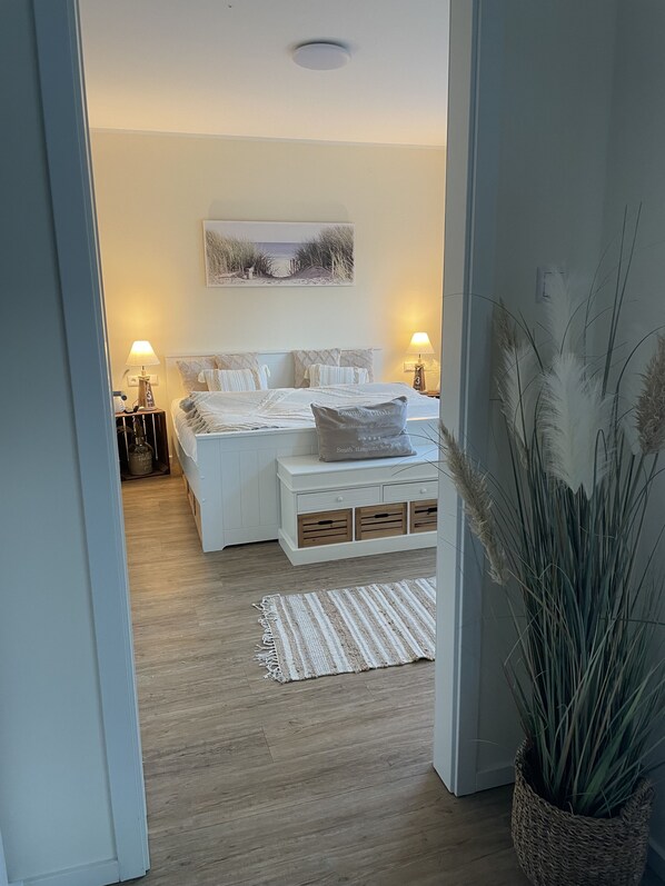 A bedroom with a bed, bedside tables, a lamp, a rug, and a plant.